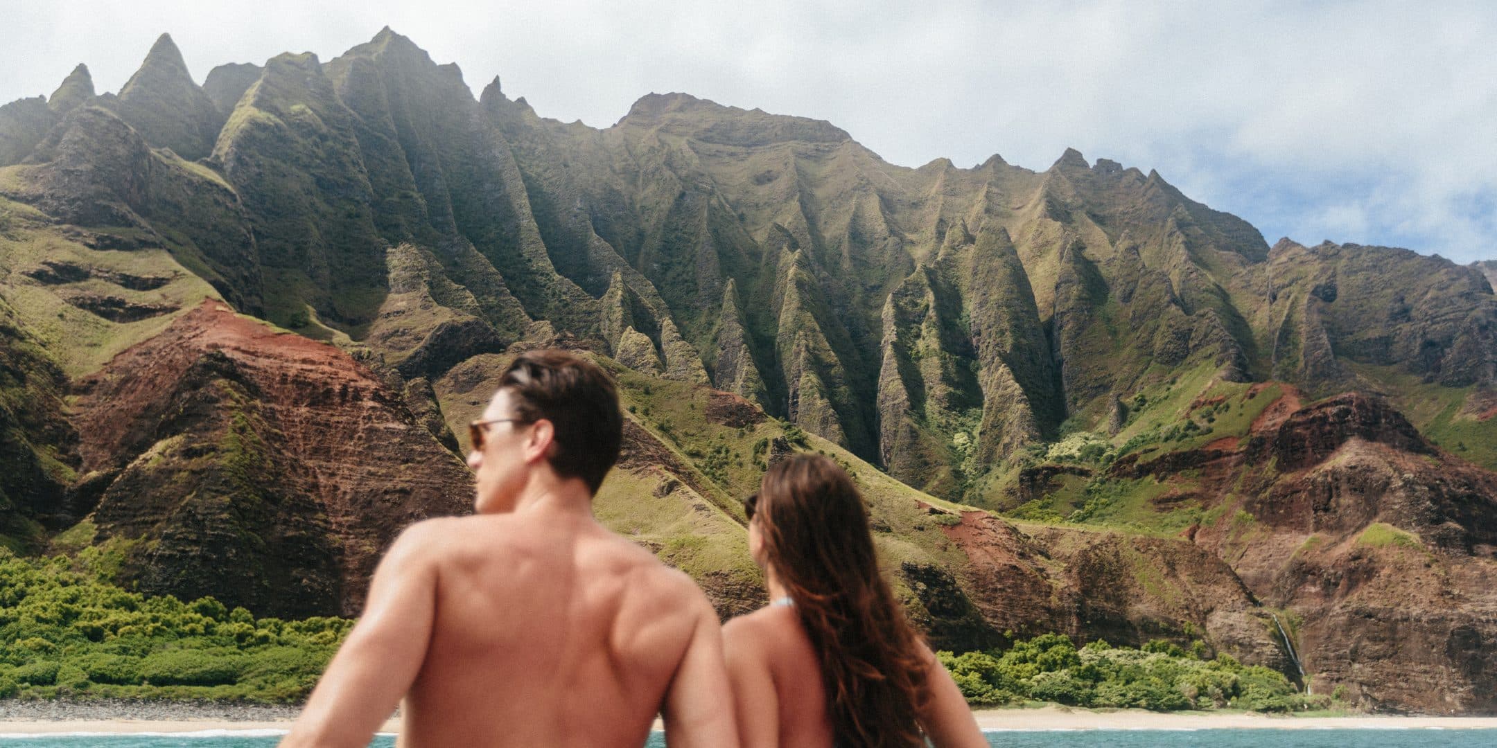 A couple on a boat looking out at the green cliffs of the Nāpali Coast