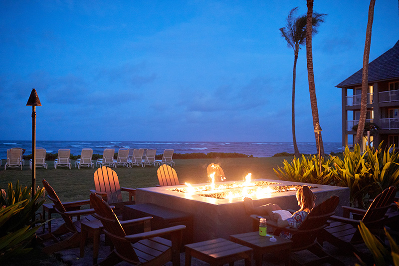 a woman sitting next to a fire pit at night